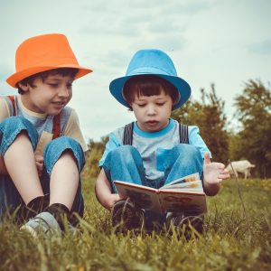 Ninos leyendo un cuento en el campo, sobre la hierba.